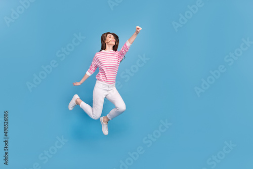 Full length profile portrait of active excited lady raise fist look empty space isolated on blue color background © deagreez