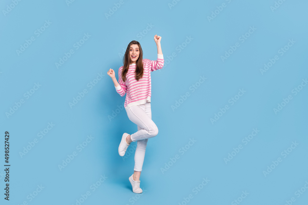 Full size photo of astonished positive lady raise fists triumph shout yeah isolated on blue color background Full size photo of astonished positive lady raise fists triumph shout yeah isolated on blue color background