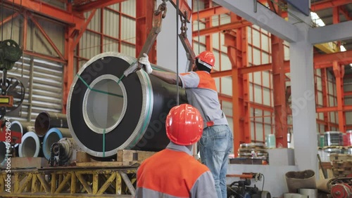 Two African workers in an industrial plant work together to bring steel hooks to lift the sheet rolls.