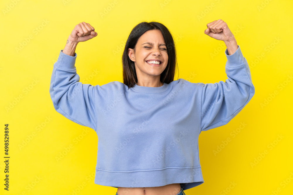 Young caucasian woman isolated on yellow background doing strong gesture - obrazy, fototapety, plakaty 