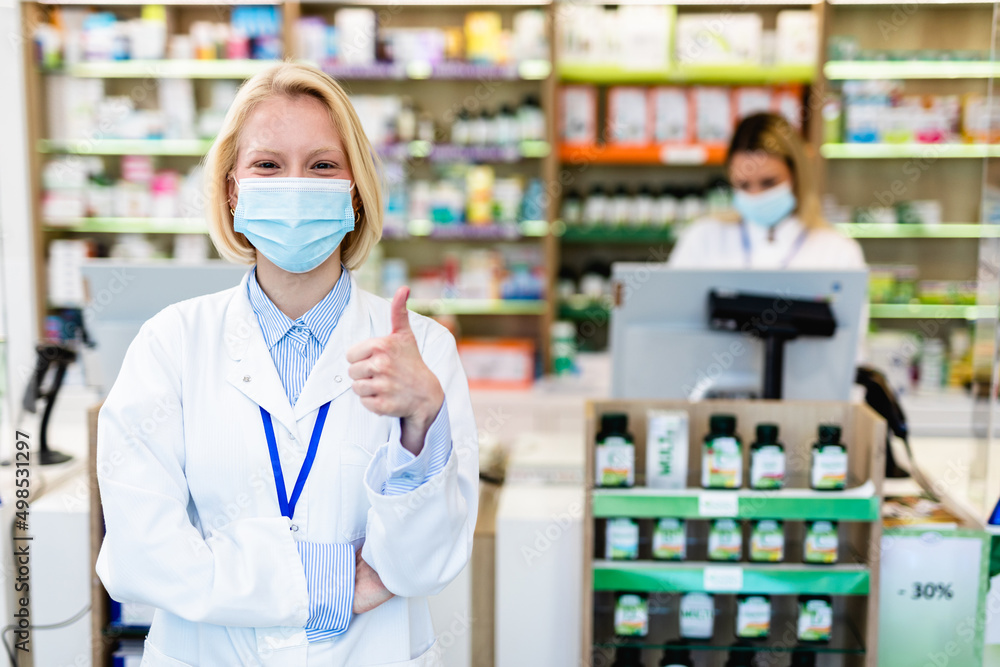 Two blond female pharmacists with protective mask on their faces working at pharmacy. Medical healthcare concept.