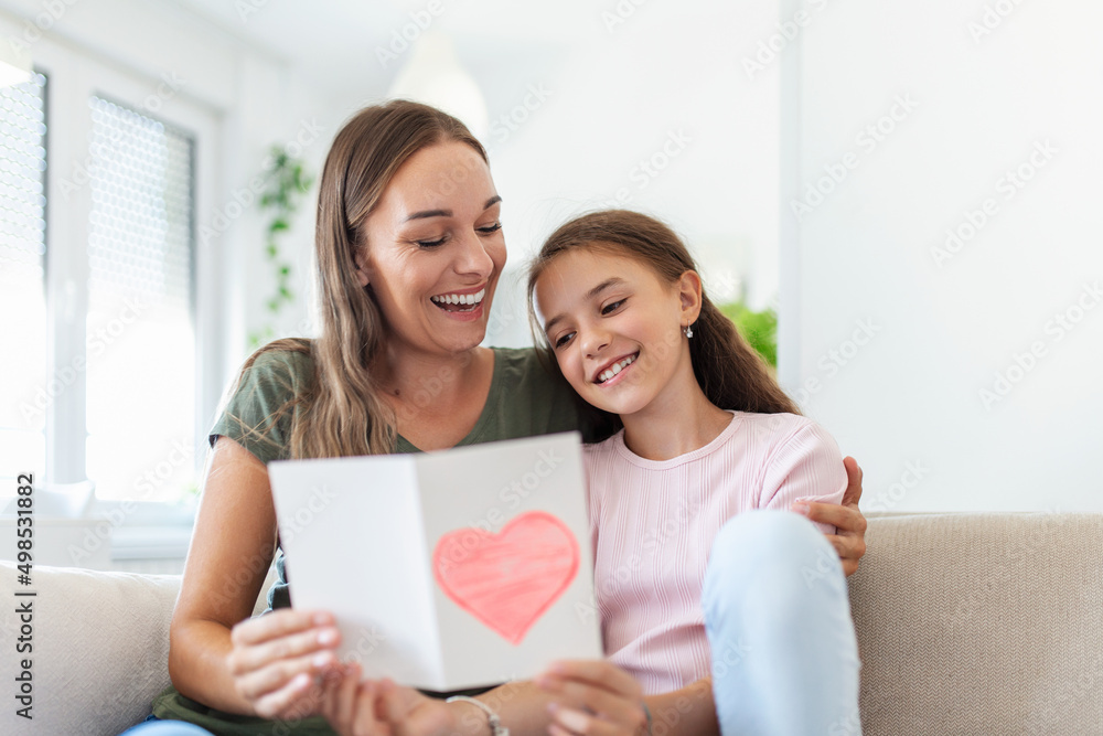Young woman and girl at home celebrating mother's day sitting on sofa daughter hugging mother kissing cheek mom laughing joyful holding gift box Young woman and girl at home celebrating mother's day sitting on sofa daughter hugging mother kissing cheek mom laughing joyful holding gift box