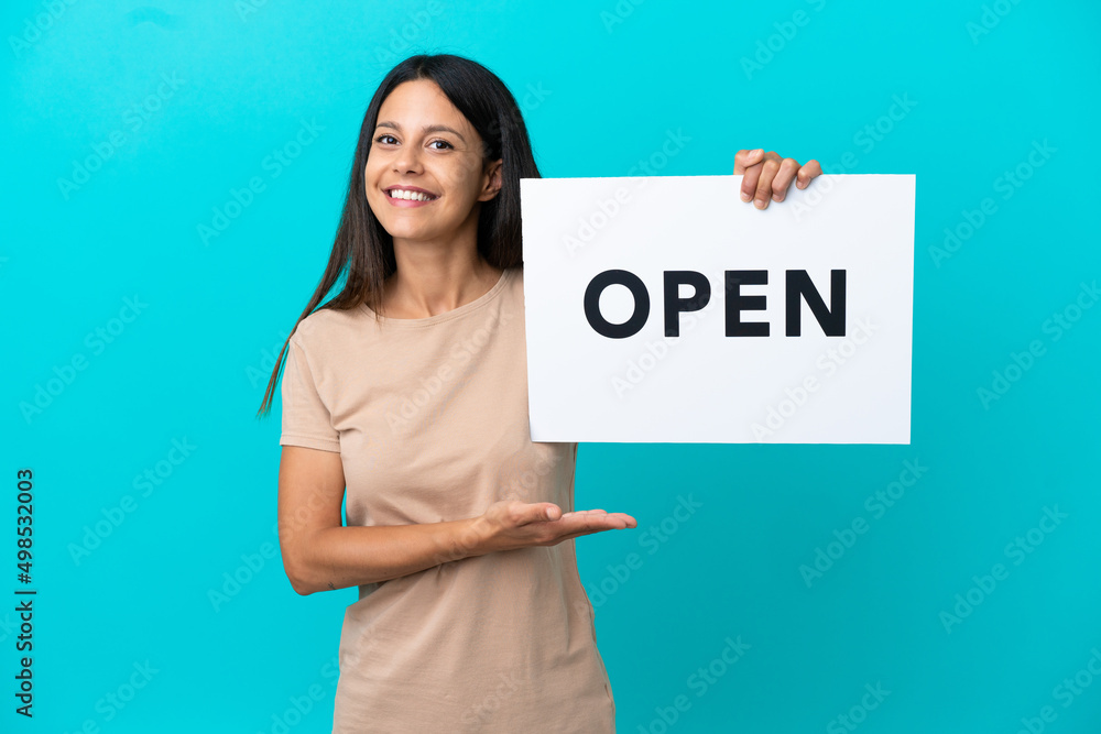 Young woman over isolated background holding a placard with text OPEN and pointing it Young woman over isolated background holding a placard with text OPEN and pointing it