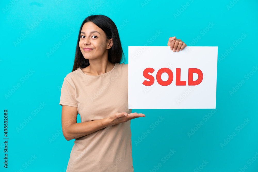 Young woman over isolated background holding a placard with text SOLD and pointing it Young woman over isolated background holding a placard with text SOLD and pointing it
