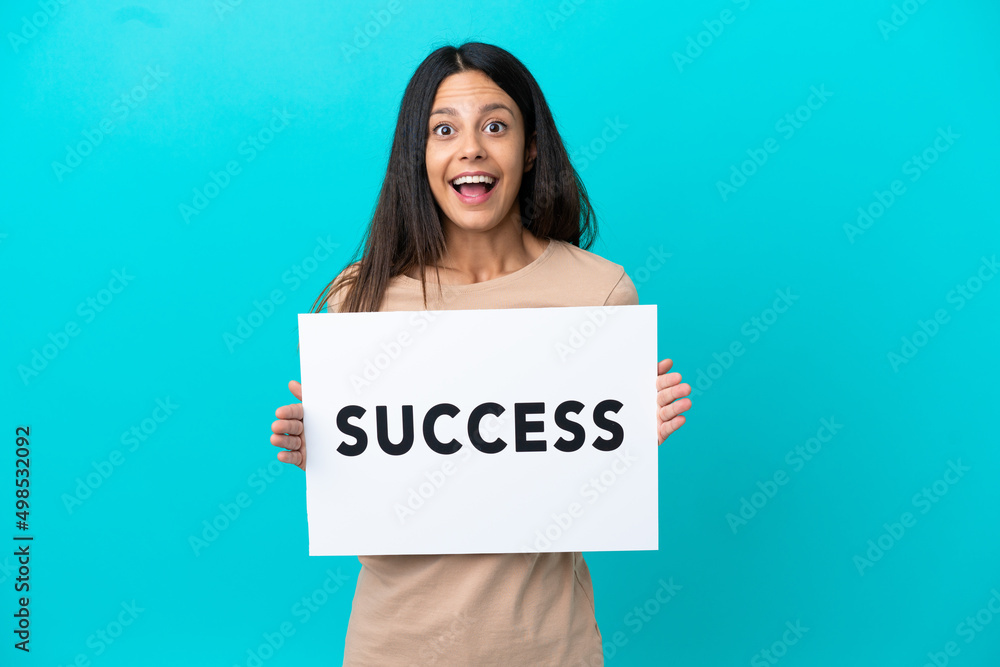 Young woman over isolated background holding a placard with text SUCCESS with surprised expression Young woman over isolated background holding a placard with text SUCCESS with surprised expression