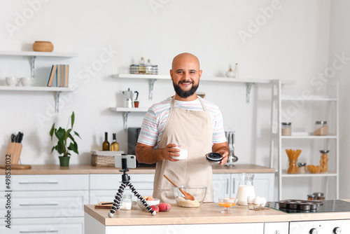 Handsome man making dough while following cooking video tutorial in kitchen