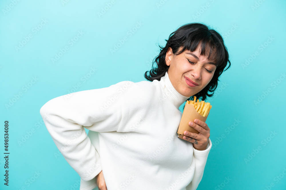 Young Argentinian woman holding fried chips isolated on blue background suffering from backache for having made an effort Young Argentinian woman holding fried chips isolated on blue background suffering from backache for having made an effort