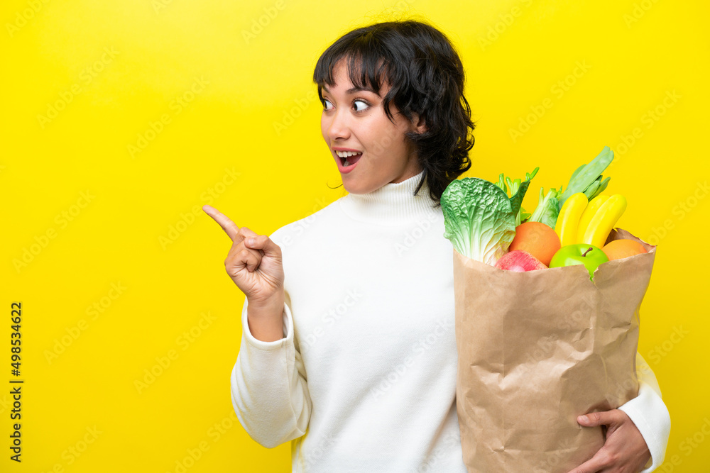 Young Argentinian woman holding a grocery shopping bag isolated on yellow background intending to realizes the solution while lifting a finger up Young Argentinian woman holding a grocery shopping bag isolated on yellow background intending to realizes the solution while lifting a finger up