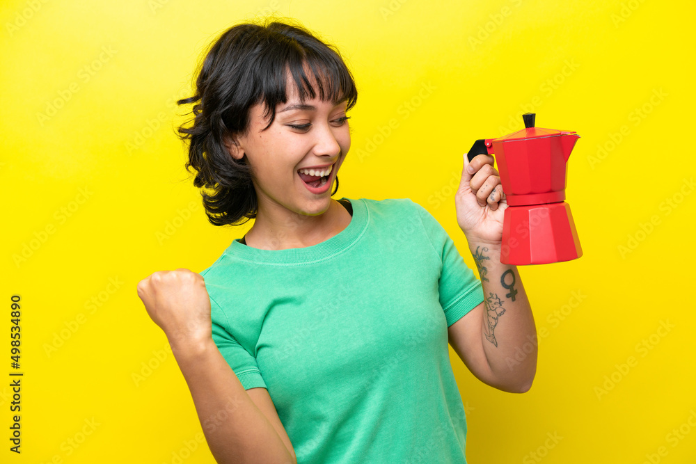 Young Argentinian woman holding coffee pot isolated on yellow background celebrating a victory Young Argentinian woman holding coffee pot isolated on yellow background celebrating a victory