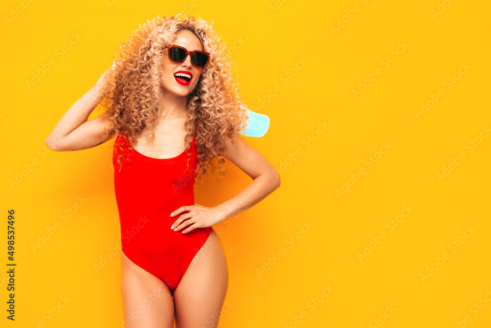 Young beautiful smiling woman posing near yellow wall in studio.Sexy model in red swimwear bathing suit.Positive female with afro curls hairstyle. Holding penny skateboard. Happy and cheerful Young beautiful smiling woman posing near yellow wall in studio.Sexy model in red swimwear bathing suit.Positive female with afro curls hairstyle. Holding penny skateboard. Happy and cheerful