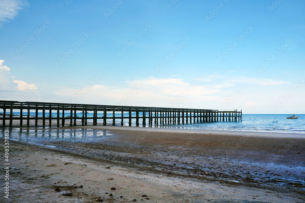 Concrete jetty that extends from the coast to the sea with beautiful sandy beach and blue sky background.