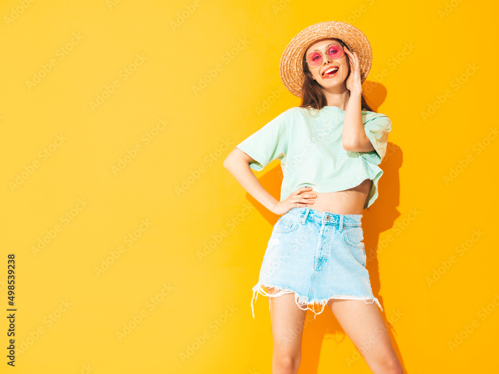 Portrait of young beautiful smiling female in trendy summer jeans skirt. carefree woman posing near yellow wall in studio. Positive model having fun indoors in sunglasses. Cheerful and happy. In hat Portrait of young beautiful smiling female in trendy summer jeans skirt. carefree woman posing near yellow wall in studio. Positive model having fun indoors in sunglasses. Cheerful and happy. In hat