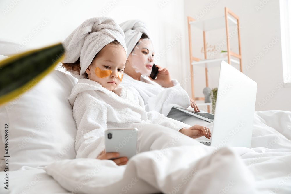 Little daughter with her working mother in bedroom