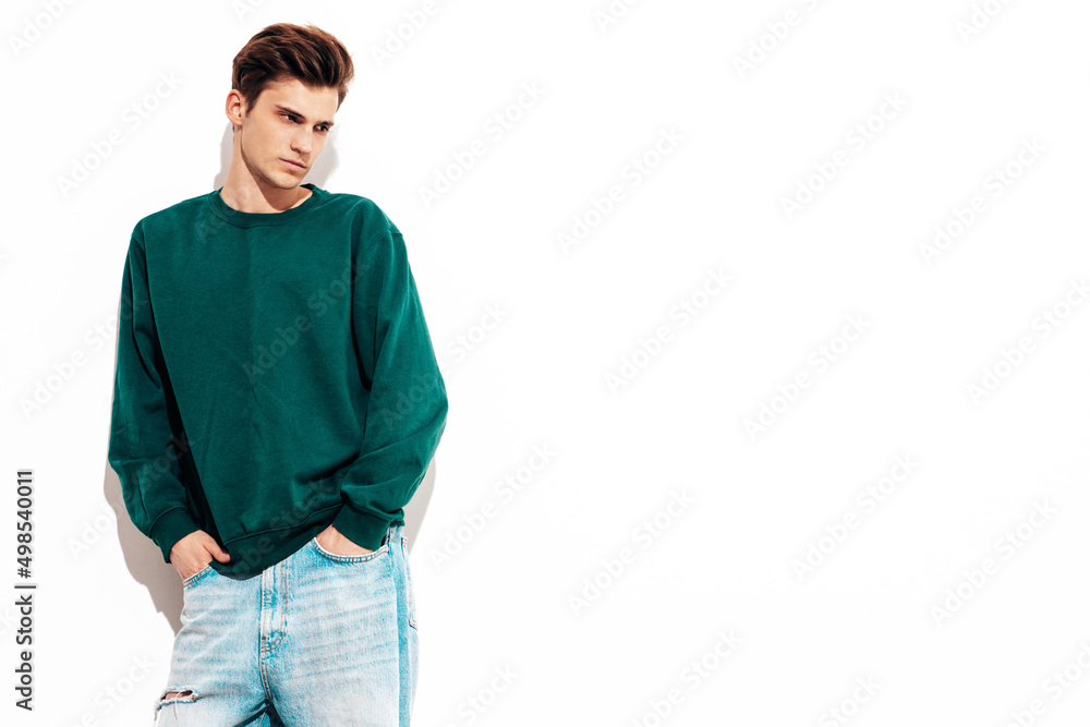 Portrait of handsome confident stylish hipster lambersexual model.Man dressed in green sweater and jeans. Fashion male posing in studio near white wall. Isolated Portrait of handsome confident stylish hipster lambersexual model.Man dressed in green sweater and jeans. Fashion male posing in studio near white wall. Isolated