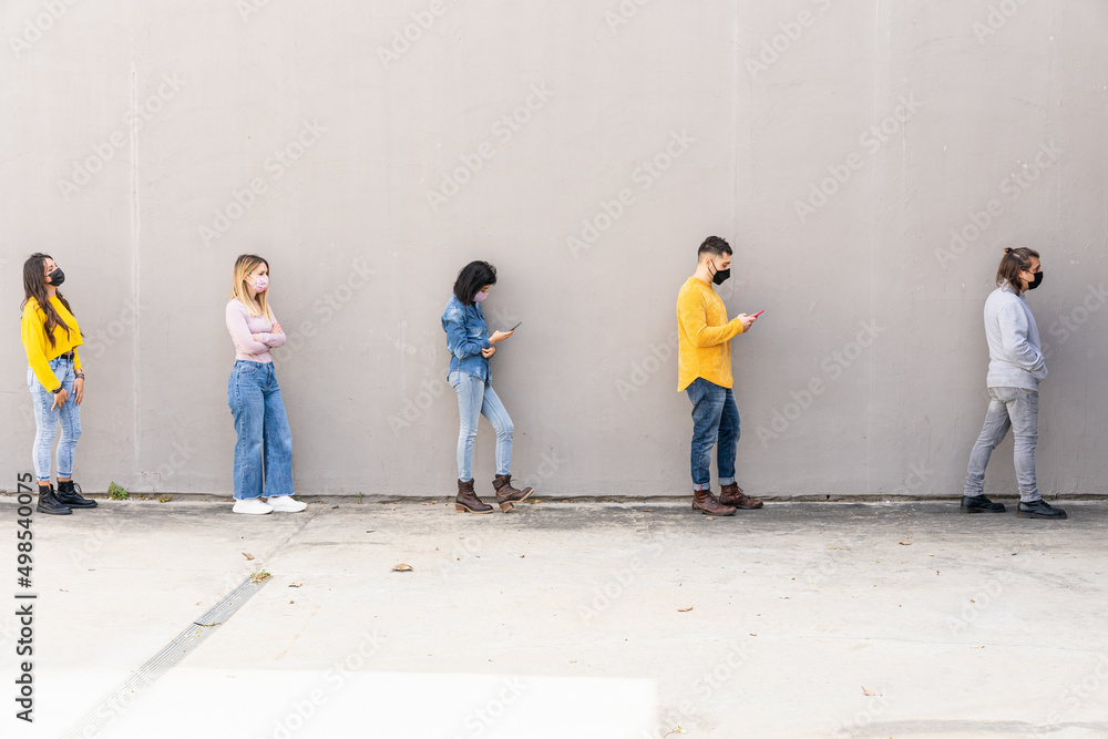 Obraz premium Group of friends at a safe distance with protective face masks against Coronavirus infections, Covid-19 - Outdoor safety concept before entering a store during the pandemic - People using smartphone