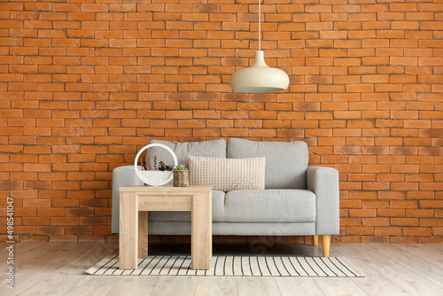 Stylish sofa and table near brick wall