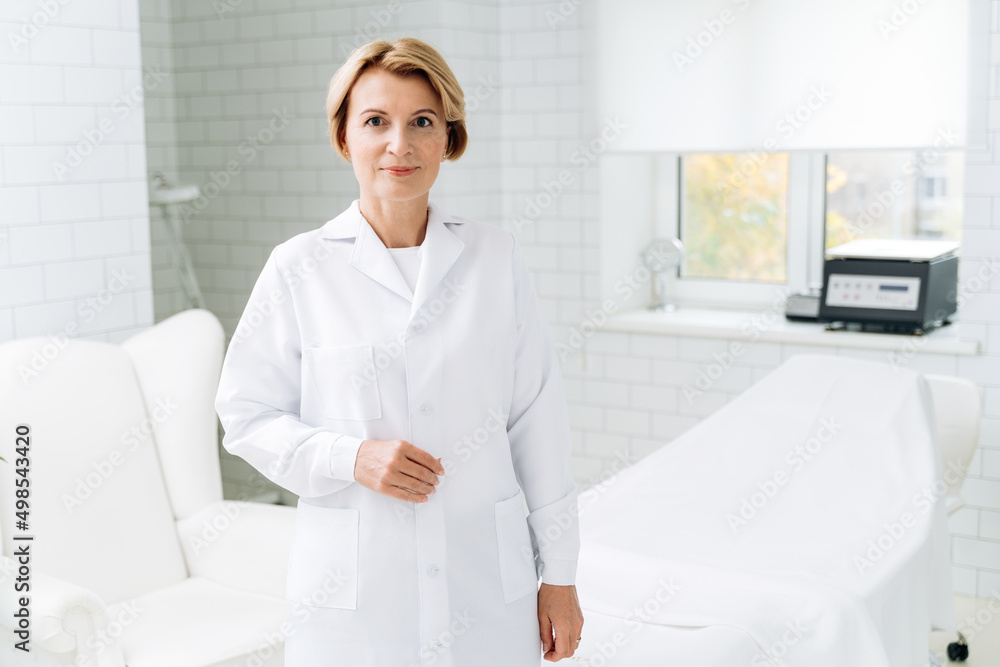 Beautician in white lab coat standing near daybed covered with sheet