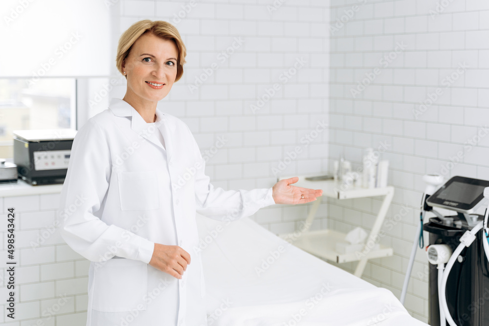 Charming beautician in white lab coat standing near daybed covered with sheet Charming beautician in white lab coat standing near daybed covered with sheet