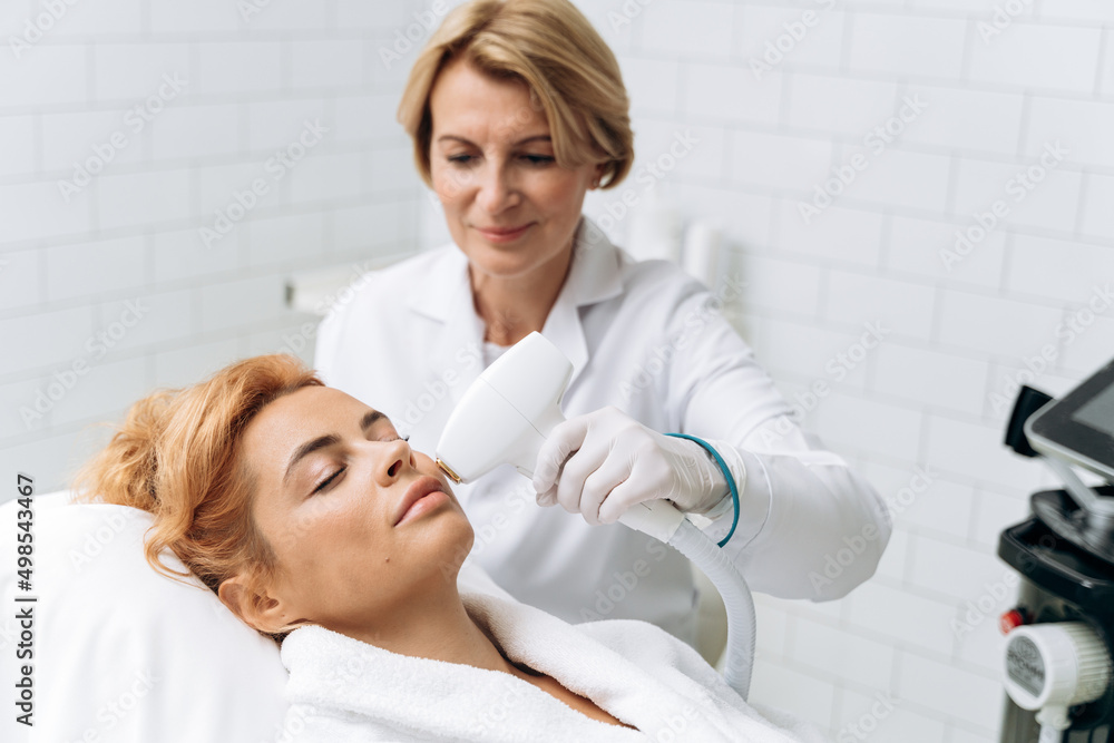 Portrait of young careful woman having laser hair removal procedure of chin zone Portrait of young careful woman having laser hair removal procedure of chin zone