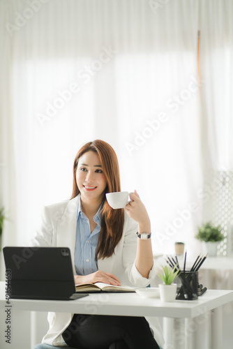 Portraits of beautiful smiling Asian women relax using laptop computer technology while sitting on their desks and using their creativity to work, work from home concept. photo