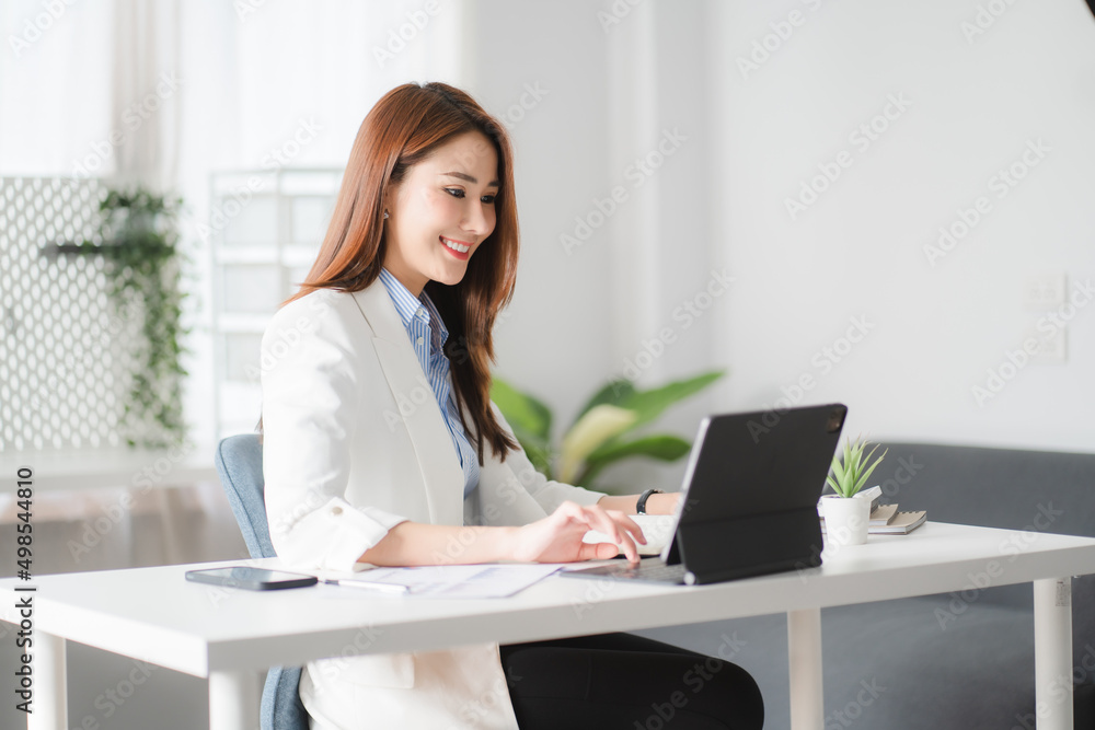 Portraits of beautiful smiling Asian women relax using laptop computer technology while sitting on their desks and using their creativity to work, work from home concept.