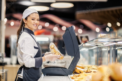 A happy bakery department saleswoman selling pastry at supermarket. photo