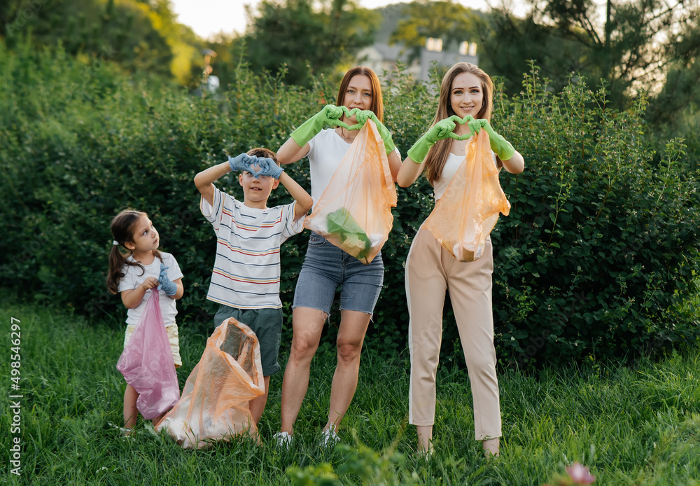 Obraz premium Young women with babies shows hearts after cleaning garbage in the park during sunset. Environmental care, waste recycling. Sorting garbage.