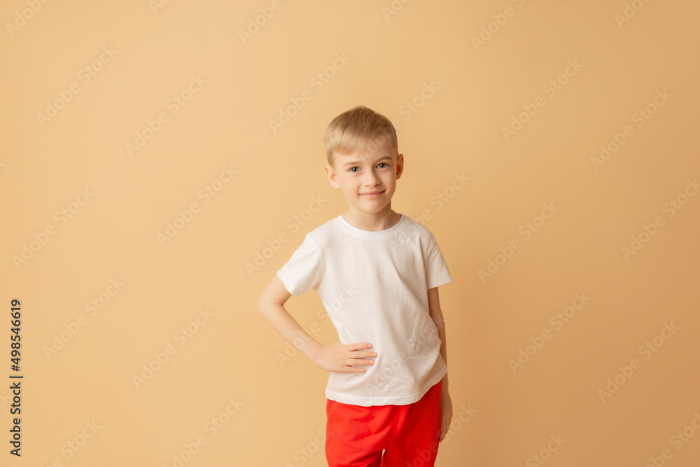 T-shirt design concept - smiling little boy in blank white t-shirt on a beige background T-shirt design concept - smiling little boy in blank white t-shirt on a beige background