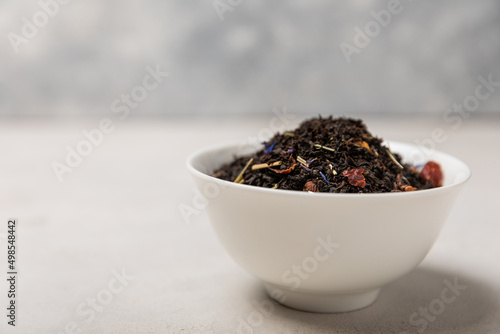 Black tea. Dried black tea leaves in a ceramic bowl. Composition with organic, natural tea on a light background. Place to copy.