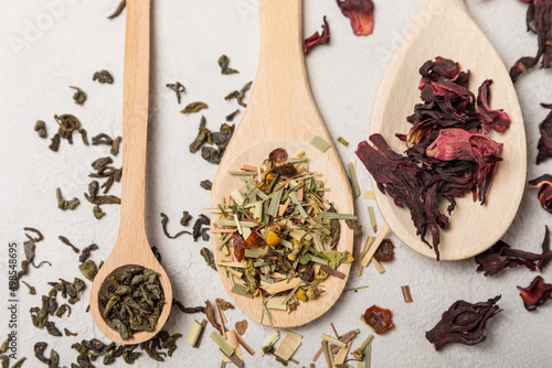 Various types of tea in wooden spoons on a light texture background. Tea mixture. Range. Black, green, herbal and hibiscus teas. Top view. Copy space.Various types of tea in wooden spoons on a light t