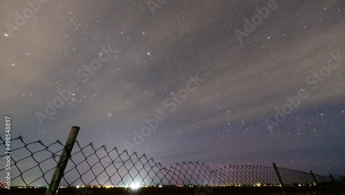 Timelapse of stars from Eastern Idaho as clouds streak through the sky looking over chainlink fence. photo