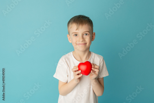 Children holding the red heart on a blue background. Concept of love, care, faith, hope, purity. Place for text. Flat fly