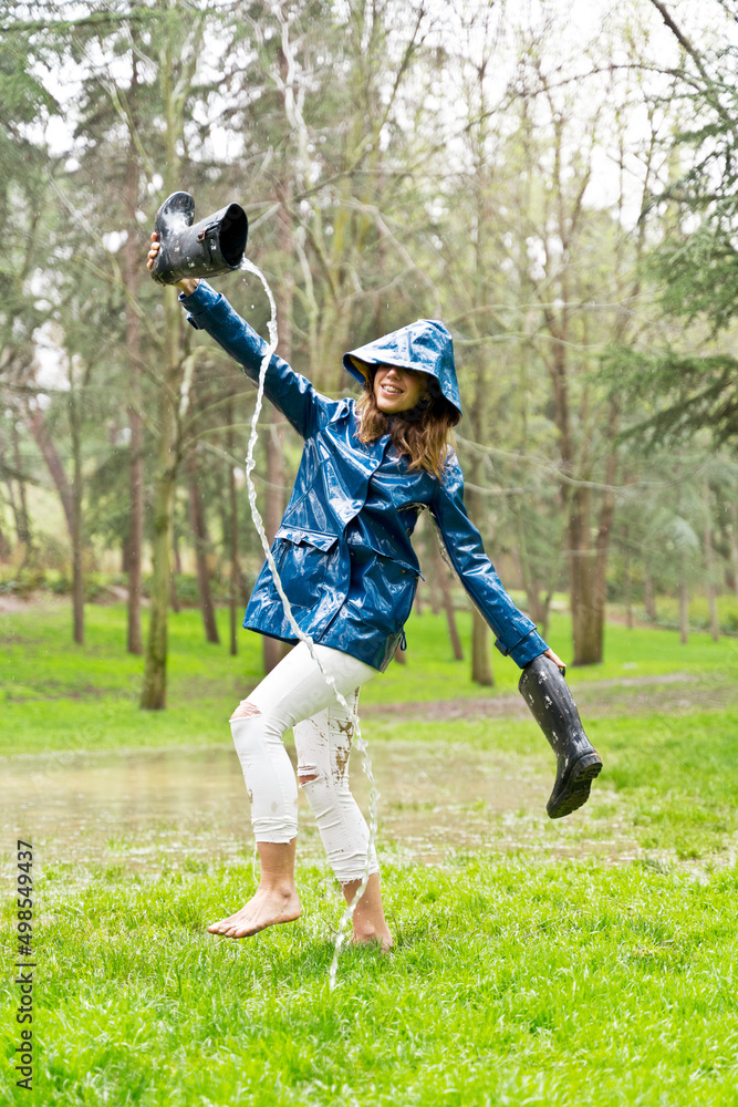 Side view of woman walking barefoot on pond empty galoshes with stream of water. Vertical panoramic view of woman splashing with mud on rainy pond. Nature and people backgrounds. Side view of woman walking barefoot on pond empty galoshes with stream of water. Vertical panoramic view of woman splashing with mud on rainy pond. Nature and people backgrounds.