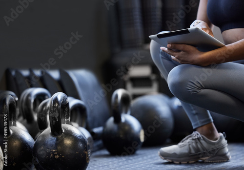 Developing a new circuit for her clients. Closeup shot of an unrecognisable woman using a digital tablet alongside kettlebells in a gym.