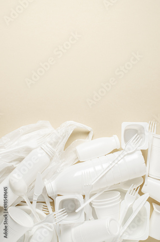 Disposable white plastic tableware on a beige background. The concept of nature pollution. Copy space.