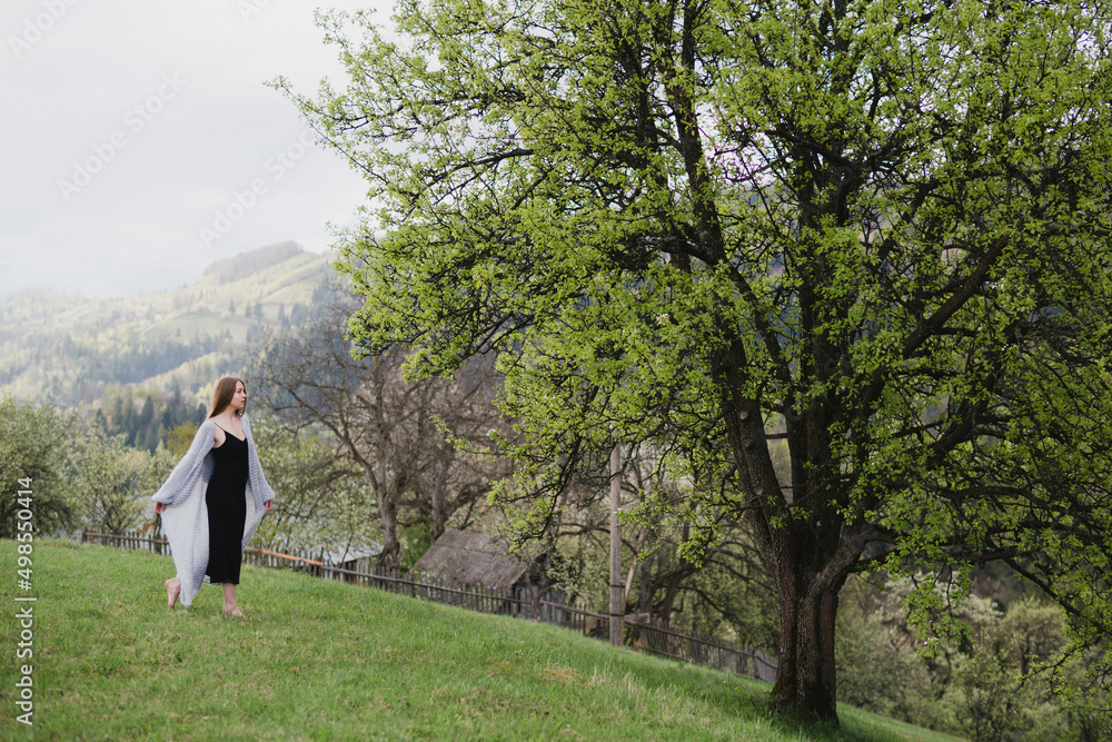 Young pretty emotional caucasian woman with long hair wearing natural makeup in romantic casual clothes walking among spring mountains near the beautiful fresh blooming tree in the countryside. Young pretty emotional caucasian woman with long hair wearing natural makeup in romantic casual clothes walking among spring mountains near the beautiful fresh blooming tree in the countryside.