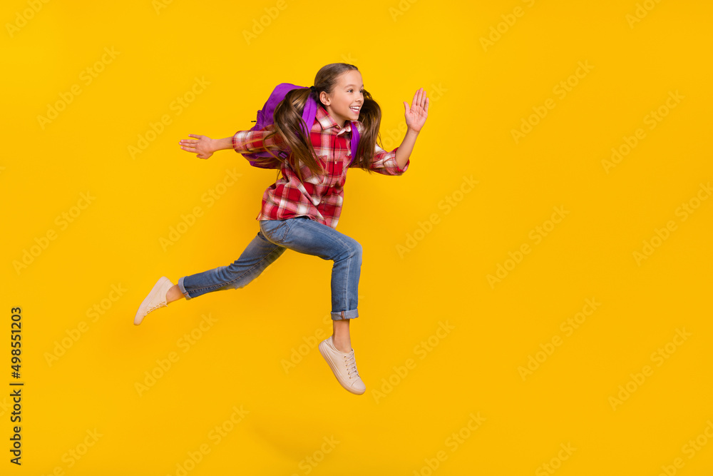 Photo of funky cute schoolgirl wear checkered shirt running fast jumping high isolated yellow color background