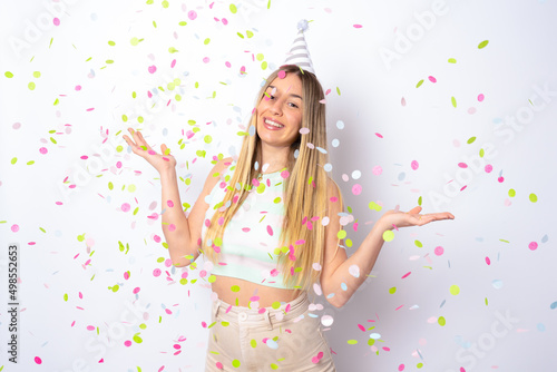 Portrait of a happy beautiful young woman standing under confetti rain and celebrating isolated over white background