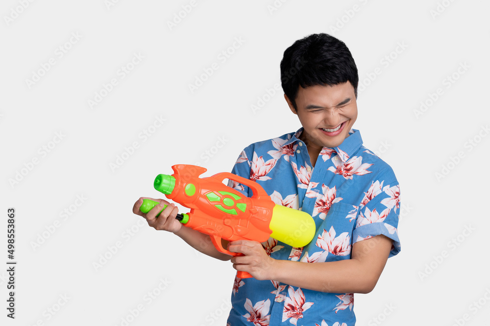 Smiling handsome Asian man playing with water gun isolated on studio blue background for Songkran festival. Smiling handsome Asian man playing with water gun isolated on studio blue background for Songkran festival.
