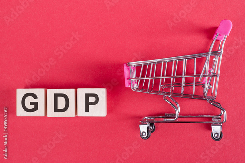 GDP - gross domestic product on cubes on a pink background next to a shopping trolley.