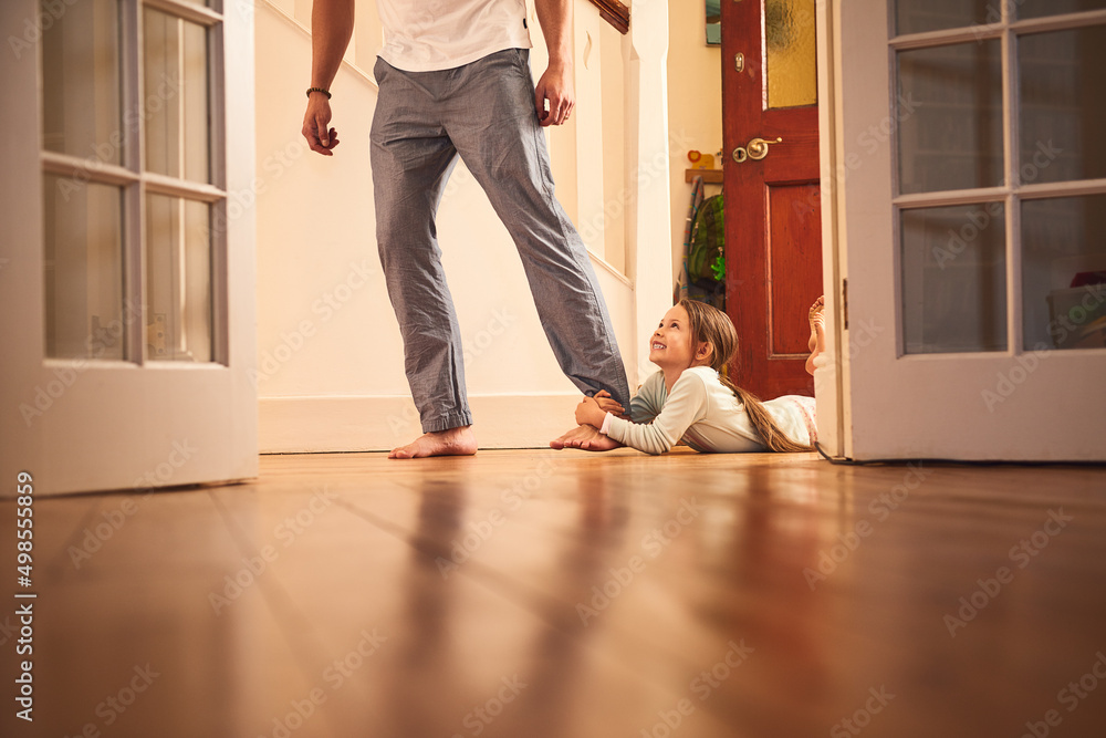 Im going with you. Shot of a cheerful little girl grabbing hold of her dads leg and not letting go while lying on the ground at home. Im going with you. Shot of a cheerful little girl grabbing hold of her dads leg and not letting go while lying on the ground at home.
