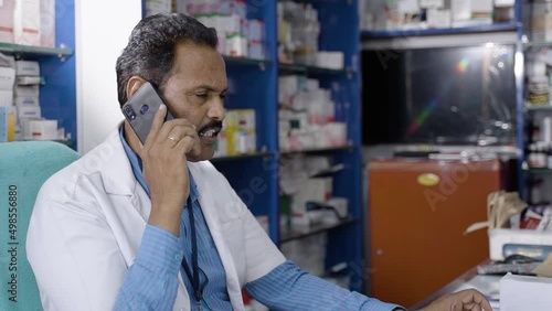 pharmacist busy speaking on mobile phone about avaliable stock while at medical store counter - concept of business communication, customer conversation and small business photo