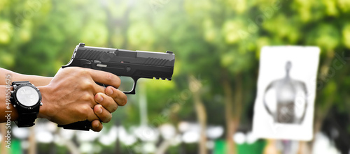 Automatic black 9mm pistol gun holding in hands of shooter and aiming to the man-target shooting paper ahead, concept for training and practising human to be body guard, vip protecting and gangsters.