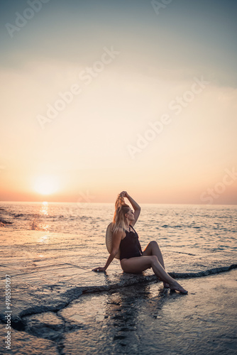 Young woman in sunglasses is resting at the sea slender in a black swimsuit. Selective focus