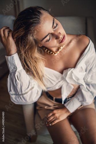Portrait of a beautiful attractive woman with blond hair sits in a room in a chair in a white shirt and beautifully posing