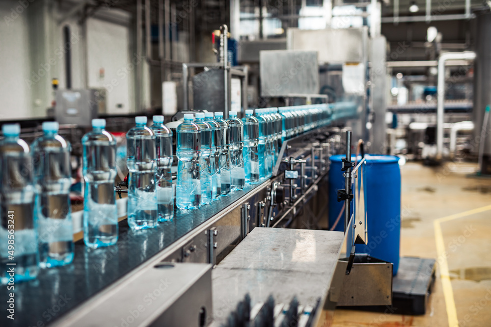 Bottling plant - Water bottling line for processing and bottling carbonated water into blue bottles. Selective focus. Bottling plant - Water bottling line for processing and bottling carbonated water into blue bottles. Selective focus.