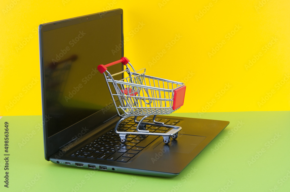 Shopping trolley on laptop on green and yellow background