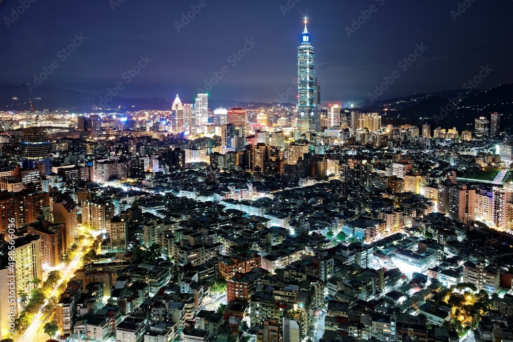 Fototapeta premium Aerial panorama over Taipei after dark, the capital city of Taiwan, with Taipei 101 Tower among skyscrapers in Xinyi Financial District, crowded buildings in downtown & city lights at night