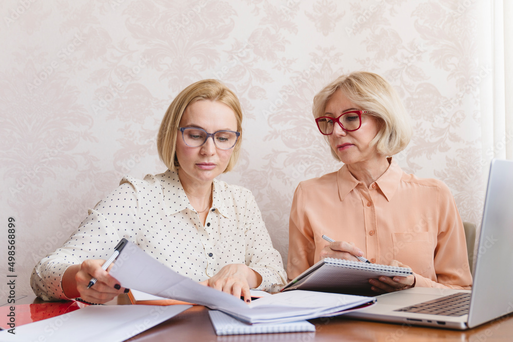 Mature business women discuss documents in the home office. Mature business women discuss documents in the home office.
