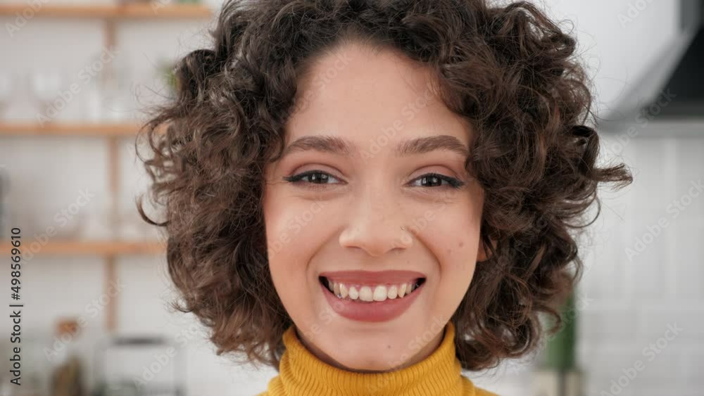 Close up face smiling hispanic curly woman looking at the camera standing at home kitchen. Headshot happy beautiful female student freelancer Close up face smiling hispanic curly woman looking at the camera standing at home kitchen. Headshot happy beautiful female student freelancer